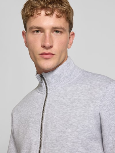 Männermodel trägt Regular Fit Sweatjacke mit Baumwoll-Anteil Modell 'Bradley' von JACK & JONES in Hellgrau, Nahaufnahme Oberkörper. Material-Mix mit Stehkragen, Reißverschluss und geteilte Känguru-Tasche.