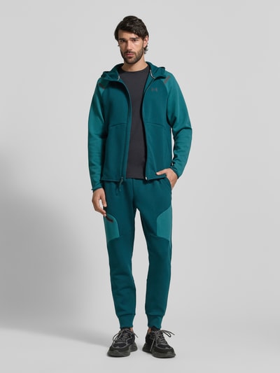 Männermodel trägt Regular Fit Sweatpants mit Logo-Print Modell 'Unstoppable' von Under Armour in Türkis mit Reißverschlusstasche, Elastischer-Material-Mix mit Baumwoll-Anteil, elastischem Bund und Beinabschlüssen, Herren, Ganzkörperansicht von vorne.