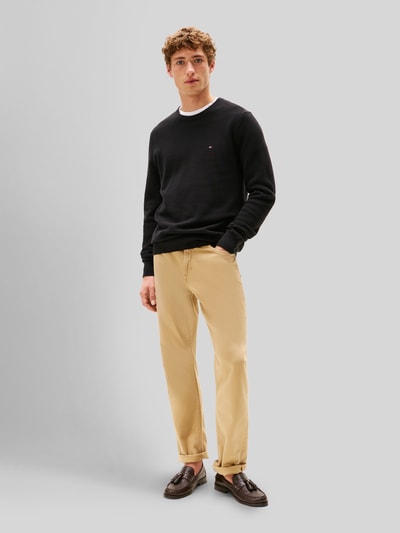 Männermodel trägt Regular Fit Strickpullover aus reiner Baumwolle von Tommy Hilfiger in Schwarz mit Strukturmuster und Logo-Detail, Ganzkörperansicht von vorne.