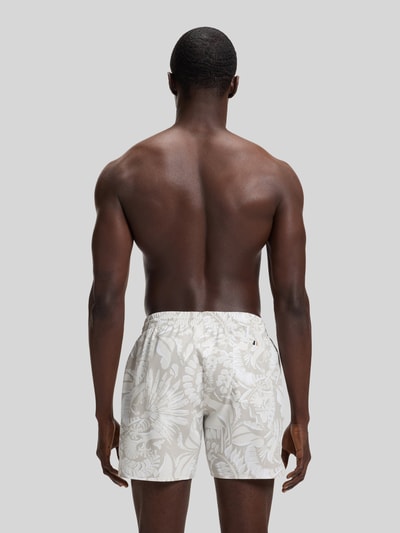 Männermodel trägt Regular Fit Badeshorts mit Allover-Muster Modell 'PIRANHA' von BOSS, florales Design, elastischer Bundabschluss mit Tunnelzug, seitliche Eingrifftaschen, Gesäßtasche mit Klettverschluss, Optik:Allover-Muster, Ganzkörperansicht Rückansicht.