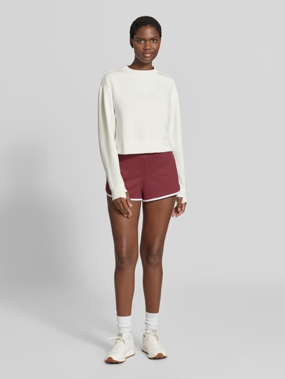 Frauenmodel trägt Cropped Sweatshirt Modell 'tasmin' von VARLEY in Creme mit Daumenschlaufen, lockere Passform, Ganzkörperansicht von vorne.