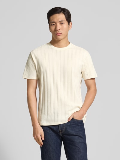 Męski model nosi Regular Fit T-Shirt aus Baumwolle od Guess, bawełniany, krój regular fit, okrągły dekolt, detal z logo, długość pleców 69 cm w rozmiarze M, kolor ecru, jednolita faktura, pełen widok z przodu.