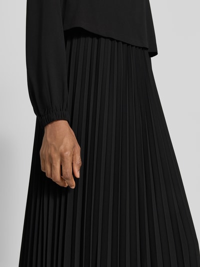 Vrouwenmodel draagt A-Linien vrijetijdsjurk met lange mouw van s.Oliver BLACK LABEL in zwart met plooien, detailopname onderlichaam.