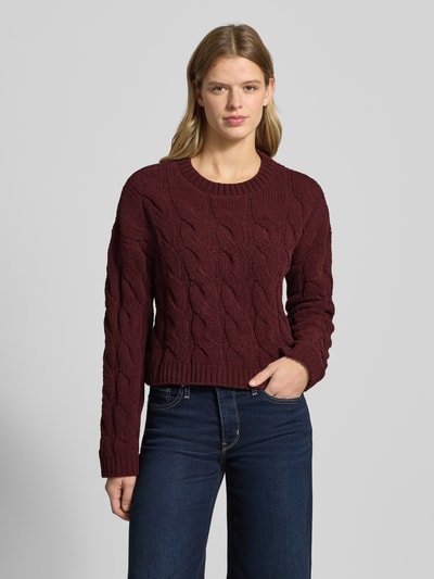 Frauenmodel trägt Regular Fit Strickpullover mit Zopfmuster Modell 'ELLY' von Only in Dunkelrot, cropped, Strukturstrick, Ganzkörperansicht von vorne