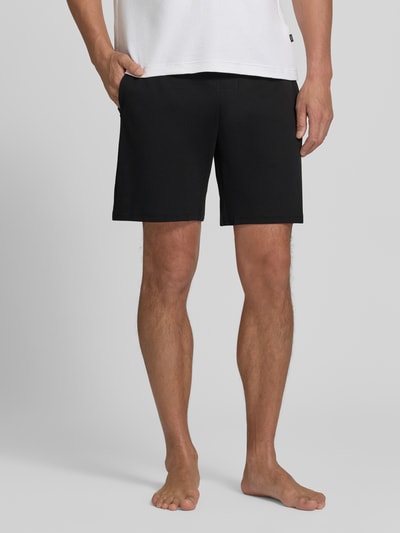 Männermodel trägt Sweatshorts aus reiner Baumwolle von Christian Berg Men in Schwarz, gerade Passform, Nahaufnahme Oberkörper bis Knie, elastischer Bund, Label-Details, Bundweite 42 cm, Innenbeinlänge 20 cm.