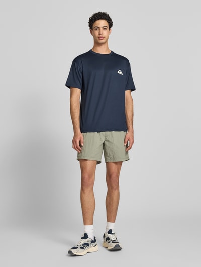 Männermodel trägt T-Shirt mit Rundhalsausschnitt und Logo von Quiksilver, Herren T-Shirt, Material-Mix mit Stretch-Anteil, Regular-Fit, Rückenlänge bei Größe M: 75 cm, Dunkelblau, Ganzkörperansicht von vorne