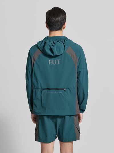 Männermodel trägt Regular Fit Jacke mit Logo-Print Modell 'Division' von HALO in Petrol und Grau, Elastischer-Material-Mix, Ganzkörperansicht Rückansicht. Rückenlänge bei Größe M: 67 cm, Schulterbreite: 40 cm, Brustweite: 54 cm, Ärmellänge: 56 cm, Regular-Fit, Stehkragen mit Kapuze, Reißverschluss, Eingrifftaschen, Elastische Ärmelabschlüsse.