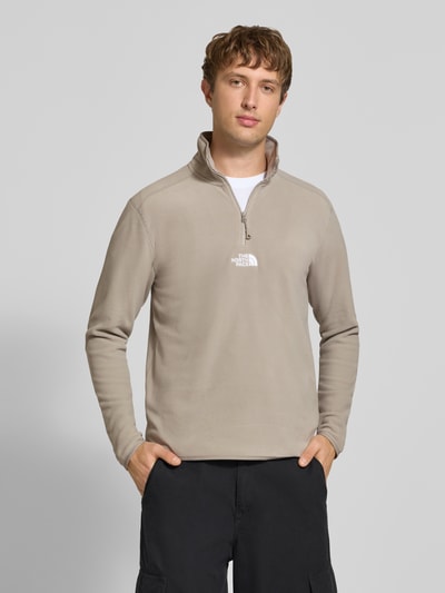 Männermodel trägt Fleecepullover mit Label-Stitching von The North Face in Beige, Regular Fit, Stehkragen, Reißverschluss, Ganzkörperansicht von vorne.