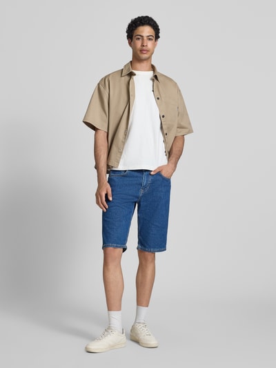 Mannelijk model draagt Regular Fit Jeansshorts uit katoenmix model 'CASH BERMUDA' van Pepe Jeans in denim-look met label patch, klinknagels, riemlussen, contrasterende stiksels, knoop- en verborgen ritssluiting, 5-pocketdesign; frontale volledig lichaamsaanzicht.