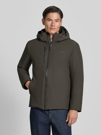 Männermodel trägt Regular Fit Jacke mit Logo-Print von Lindbergh, elastyczna mieszanka materiałów, kaptur z tunelem, napoleońska kieszeń, kolor ciemny, gładka tekstura, Ganzkörperansicht von vorne. Szerokość w rozmiarze M: 42 cm, długość tyłu w rozmiarze M: 74 cm, szerokość ramion w rozmiarze M: 46 cm, długość rękawów w rozmiarze M: 62 cm.