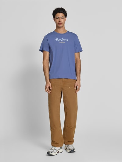 Męski model nosi Regular Fit T-Shirt aus reiner Baumwolle Modell 'EGGO' von Pepe Jeans, jednokolorowy, nadruk z logo, naszywka z logo, okrągły dekolt, krótki rękaw, dżersej, bawełna, Ganzkörperansicht von vorne.