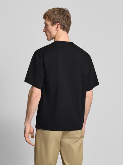 Männermodel trägt T-Shirt mit Label-Detail und Rundhalsausschnitt von Dickies in Schwarz, Relaxed Fit, reine Baumwolle, Rückenlänge 70 cm, Ganzkörperansicht Rückansicht.