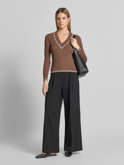 Frauenmodel trägt Slim Fit Pullover aus Viskose-Mix in Strick-Optik von ARMANI EXCHANGE, braune Farbe, V-Ausschnitt, breite und elastische Abschlüsse, schwarze weite Hose, Glattledertasche, glatte Textur, Rückenlänge bei Größe S 55 cm, Ärmellänge 59 cm, Ganzkörperansicht von vorne.