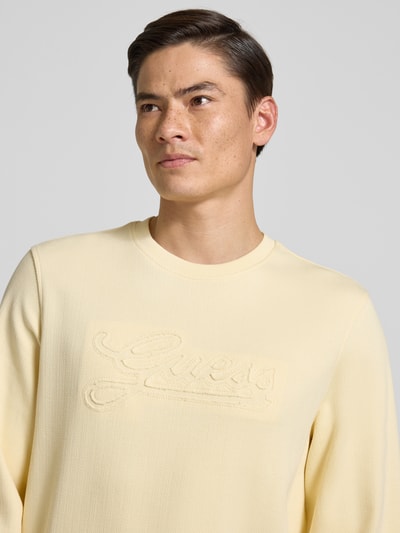 Männermodel trägt Sweatshirt mit Logo und Rundhalsausschnitt von Guess aus reiner Baumwolle in Gelb, Regular Fit, Nahaufnahme Oberkörper.