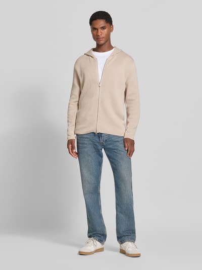 Męski model nosi Regular Fit Pullover aus reiner Baumwolle von Marc O'Polo, beżowy sweter z bawełny, proste niebieskie jeansy, białe buty, jasnoszare tło, Ganzkörperansicht von vorne.
