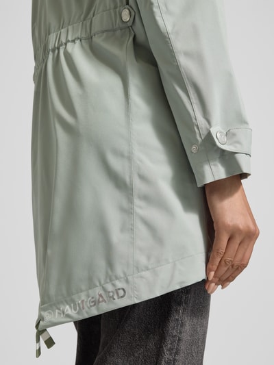 Frauenmodel trägt Jacke mit Ärmelriegeln von NAUTGÅRD in hellem Grün mit Reißverschlusstaschen und Markenlogo, Nahaufnahme Oberkörper. Regular Fit, Kapuze mit Tunnelzug, Schulterbreite 45 cm, Brustweite 51 cm, Rückenlänge 90 cm, Ärmellänge 62 cm.