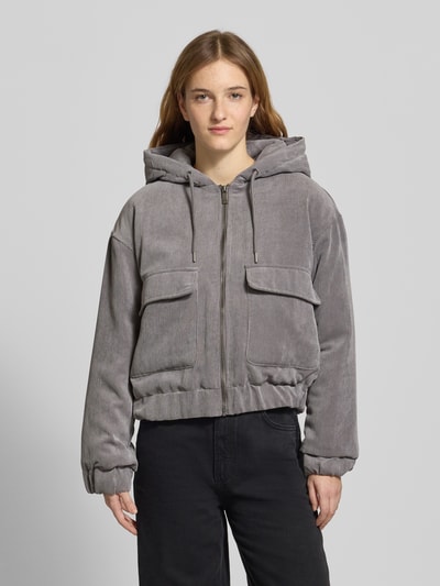 Frauenmodel trägt Regular Fit Bomberjacke mit Kapuze Modell 'SUVA' von Only, grau, Cord, aufgesetzte Taschen, Ganzkörperansicht von vorne.