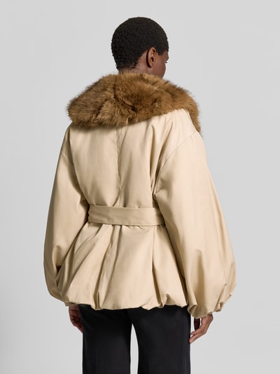 Frauenmodel trägt Jacke mit Kunstfellbesatz von ROTATE in Beige mit braunem Kunstfellkragen, taillierter Passform und elastischen Ärmelabschlüssen, Rückenansicht, Material-Mix mit Baumwoll-Anteil, Taillienband, KI-modifiziertes Bild.