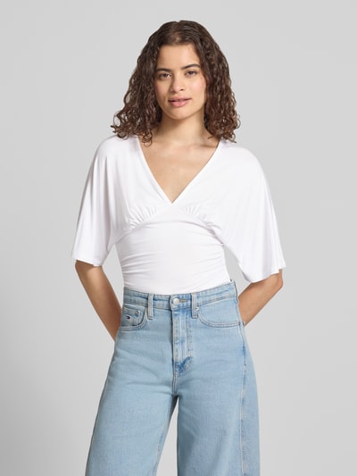 Frauenmodel trägt Bluse aus Viskose-Mix mit V-Ausschnitt von Gina Tricot in Weiß, taillierte Passform, Halbarm, Ganzkörperansicht von vorne.