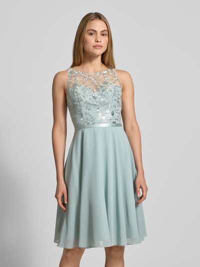 Frauenmodel trägt Cocktailkleid mit floraler Stickerei von LUXUAR FASHION, Gerader-Schnitt, Knielänge, Paillettenbesatz, Rundhalsausschnitt, wattierte Cups, Nahtreißverschluss, Rückenlänge 96 cm, Brustweite 38 cm, Ganzkörperansicht von vorne.