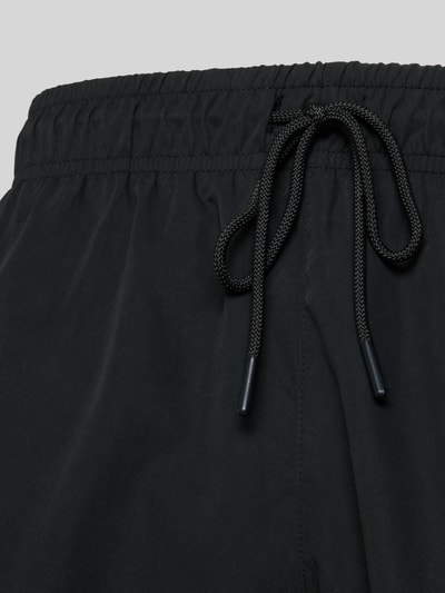 Produktfoto, schwarze Badeshorts mit Logo-Stitching von Lacoste, elastischer Bund, Tunnelzug, seitliche Taschen, glatte Textur, schnelltrocknend.
