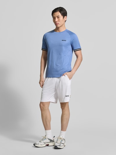 Männermodel trägt Regular Fit T-Shirt mit Label Print Modell 'TOC SERVE 2' von BOSS Green in Hellblau mit Logo- und Kontrastdetails, Ganzkörperansicht von vorne.