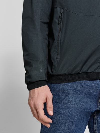 Männermodel trägt Jacke mit Kapuze Modell 'KOS' van Killtec in zwart met rits, label-patch, zijritszakken, elastische mouwuiteinden, detailopname onderarm