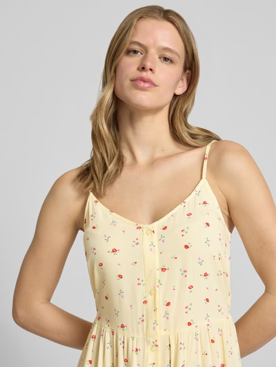 Frauenmodel trägt Leicht ausgestelltes Minikleid aus reiner Viskose Modell 'TALA' von Pieces, Optik:Allover-Muster, floral, V-Ausschnitt, verstellbare Spaghettiträger, ohne Ärmel, Material: Viskose, sanfte Gelbtöne mit kleinen Blumen, Nahaufnahme Oberkörper.
