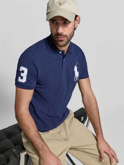 Mannelijk model draagt Shaped Fit Poloshirt uit puur katoen van Polo Ralph Lauren, effen blauw, logo-stitching, piqué structuur, kortemouw, polokraag, asymmetrische zoom, voorkant, close-up bovenlichaam.