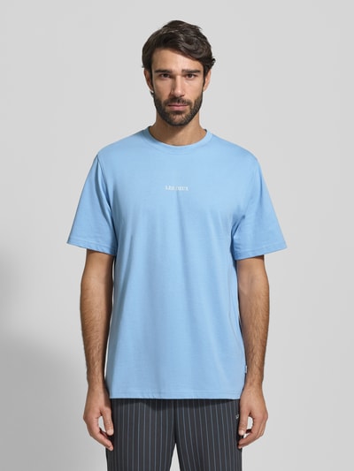 Männermodel trägt hellblaues Herren T-Shirt mit Rundhalsausschnitt Modell 'Andrew' von Les Deux, reine Baumwolle, Regular-Fit, Logo, Ganzkörperansicht von vorne. Rückenlänge bei Größe M: 71 cm.