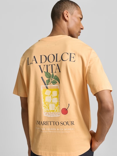 Mannenmodel draagt T-Shirt met rückseitigem Motiv-Print van MCNEAL in lichte oranje kleur met grote print, rechte fit, ronde hals, ruglengte 70 cm, ganzkörperansicht rückansicht.