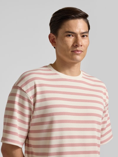 Männermodel trägt Oversized T-Shirt mit Rundhalsausschnitt Modell 'Gael' von Redefined Rebel, Elastischer-Material-Mix, Oversized-Fit, rosa-weiß gestreift, Nahaufnahme Oberkörper.