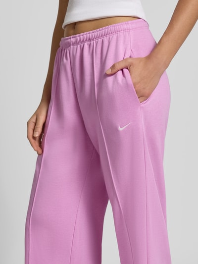 Kobieta nosi Wide Leg Sweathose aus Baumwoll-Mix od Nike, różowa tkanina, elastyczny pas, gładka faktura, zbliżenie na biodra.