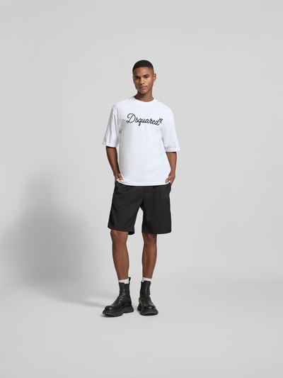 Männermodel trägt Loose Fit T-Shirt aus reiner Baumwolle von Dsquared2 in Weiß mit schwarzem Label-Stitching, Ganzkörperansicht von vorne. Herren T-Shirt, Rundhalsausschnitt, verlängerte Rückseite, Rückenlänge bei Größe M: 67 cm.