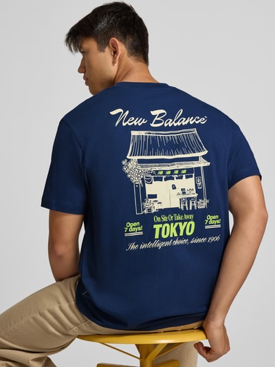Männermodel trägt Regular Fit T-Shirt aus reiner Baumwolle mit Label-Detail von New Balance in Dunkelblau, Rückenansicht, Nahaufnahme Oberkörper. Modell 'GRAB A BITE TOKYO', Rückenlänge bei Größe M 70 cm, Grafikdruck auf Rückseite.