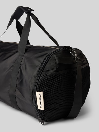 Produktfoto, schwarze Duffel Bag mit Logo-Detail von AY STUDIOS, Reißverschlussfächer außen und innen, verstellbarer Schulterriemen, Nylonstruktur, 54x32x30 cm, Schulterriemen 94 cm.