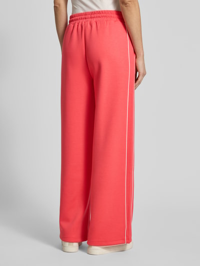 Frauenmodel trägt Wide Fit Sweatpants mit elastischem Bund Modell 'KATE NEO' von ICHI in Koralle, weiche Textur, Ganzkörperansicht Rückansicht. Material-Mix mit Viskose-Anteil und Tunnelzug, Kontrastpaspelierung sichtbar.