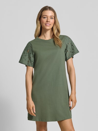 Frauenmodel trägt Leicht ausgestelltes Freizeitkleid aus reiner Baumwolle Modell 'VILLA' von Vero Moda, Optik: Unifarben in Oliv, Spitzenbesatz an Kurzarm, Mini-Länge, Jersey Materialverarbeitung, Ganzkörperansicht von vorne.
