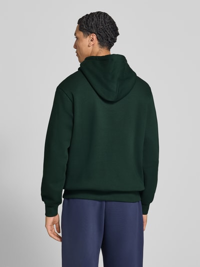 Männermodel trägt Hoodie aus Baumwoll-Mix Modell 'FREDERIKS' von JACK & JONES in Dunkelgrün, lockere Passform, Ganzkörperansicht Rückansicht.