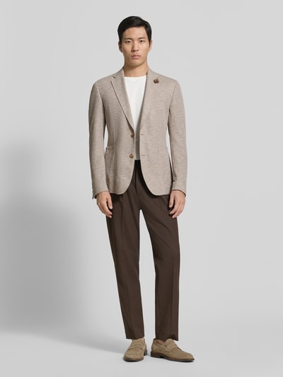 Männermodel trägt Regular Fit Blazer mit floraler Applikation Modell 'Hoverest' von JOOP! Collection aus Baumwoll-Mix in Beige mit Strukturmuster, 2-Knopfleiste, Brusttasche, Reverskragen und aufgesetzten Taschen, Ganzkörperansicht von vorne.