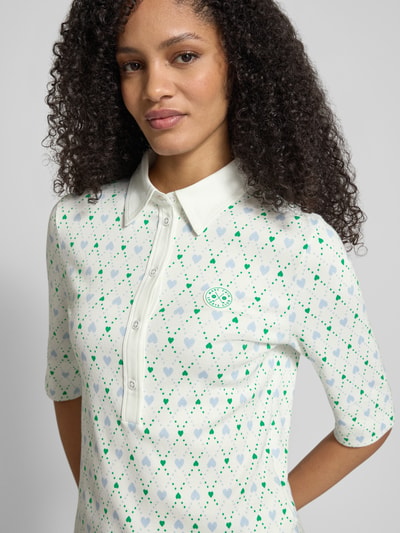 Frauenmodel trägt Slim Fit Poloshirt mit Logo-Applikation von Marc Cain aus elastischem Baumwoll-Mix mit Allover-Motiv-Print, Halbarm, Polokragen, Nahaufnahme Oberkörper.
