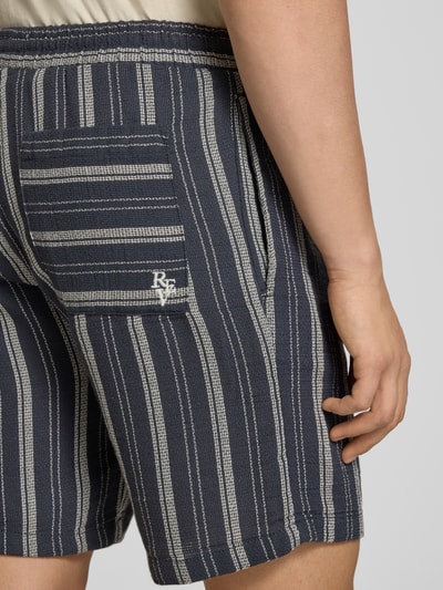 Mężczyzna nosi Shorts mit elastischem Bund und Logo-Detail von REVIEW, bawełniany materiał w prążki, krój regular fit, szerokość w rozmiarze M 42 cm, długość nogawki 20 cm, detal logo, widok z tyłu, zbliżenie na biodra.