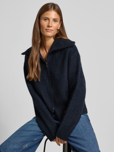 Frauenmodel trägt Strickjacke aus Mohair-Mix mit Label-Detail Modell 'Hulda' von MOS MOSH in Dunkelblau, lockere Passform, Nahaufnahme Oberkörper. Damen Strickjacke mit Stehkragen, Zweiwege-Reißverschluss, gerippter Bund, Rückenlänge 53 cm, Ärmellänge 60 cm, Mohair-Mix mit Lanawoll-Anteil.