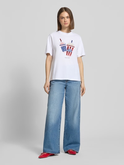 Frauenmodel trägt Damen T-Shirt Regular Fit T-Shirt aus reiner Bio-Baumwolle Modell 'BURST' von Only mit Optik: Unifarben, Paillettenbesatz, Rundhals, Kurzarm, Jersey, in Weiß, kombiniert mit blauen Jeans und roten Schuhen, Ganzkörperansicht von vorne.