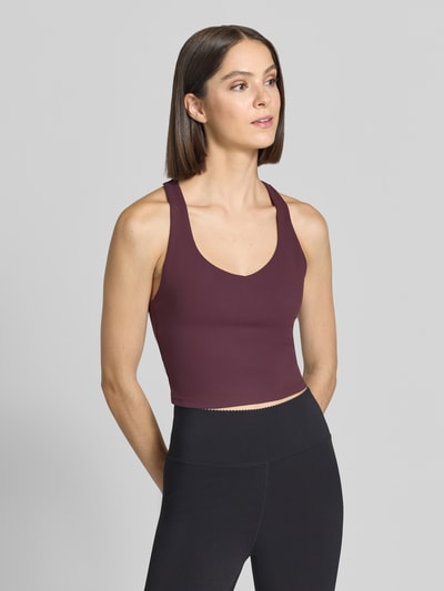 Vrouwenmodel draagt Cropped Top met geïntegreerde cups van Fabletics in bordeaux met zwarte slim fit broek, ronde hals, ruglengte maat S 36 cm, dames top, nahaufnahme bovenlichaam.