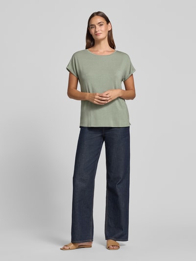 Frauenmodel trägt Relaxed Fit T-Shirt aus Viskose-Mix von Christian Berg Woman in zartem Grün mit Glitzer-Optik, Ganzkörperansicht von vorne. Rückenlänge bei Größe S 63 cm, elastischer Viskose-Mix, Damen T-Shirt mit Rundhalsausschnitt.