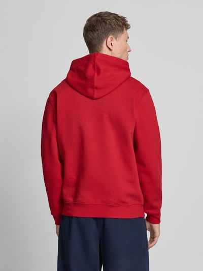 Männermodel trägt hoodie met kangoeroezak van GAP in rood katoenmix met ribboorden, labelstitching, los model, ruglengte 69 cm, mouwlengte 65 cm, geheel van achteren.