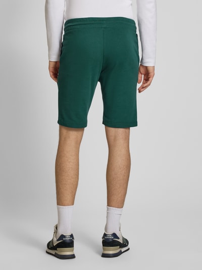 Männermodel trägt Shorts mit Logo-Print Modell 'GORDON' von Jack & Jones aus Baumwoll-Mix in Grün, Relaxed-Fit, Ganzkörperansicht Rückansicht.
