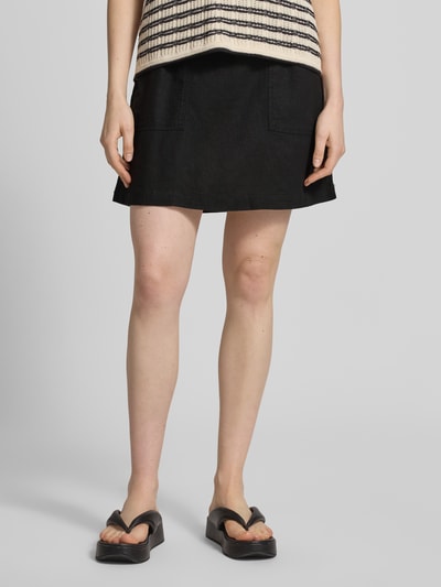Frauenmodel trägt Minirock aus Leinen-Viskose-Mix Modell 'LINNO' von ICHI in Schwarz, A-Linie, elastischer Bund, Allover-Look, Nahaufnahme Unterkörper. Bundweite bei Größe 36: 38 cm, Gesamtlänge bei Größe 36: 43 cm.