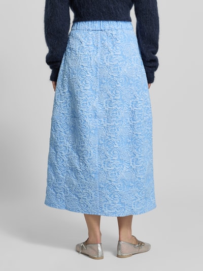 Kobiece modelka nosi spódnica midi w wzór na całej powierzchni model 'ROSIE' od Copenhagen Muse, linia a, elastyczny pas, szerokość w rozmiarze S: 37 cm, całkowita długość w rozmiarze S: 82 cm, niebieski, teksturowany materiał, widok całej sylwetki z tyłu.